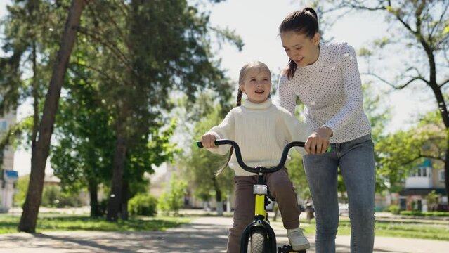 happy mother teaches little Child ride bicycle. Little daughter girl dreams traveling by bike. Walk park. Happy family. Kid rides his bike through park for first time. Mom Child Bike. drive bicycle
