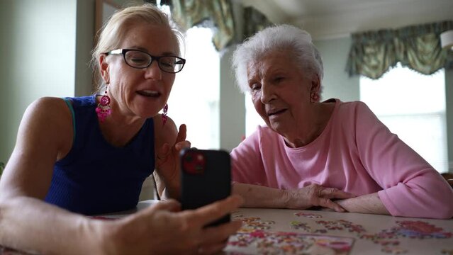 Low angle view of happy waving and smiling elderly senior woman with mature middle aged daughter, have video chat on phone. Smiling talking to family on smartphone. Generative AI