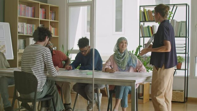 Full shot of female teacher questioning multi-ethnic immigrant students while giving lesson in language school