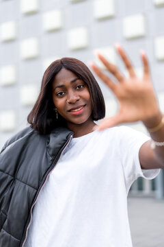 Fashion portrait of young black woman with a gray building in the background. Wearing a white shirt and black pants, lifestyle photos