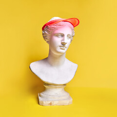 Antique statue bust wearing stylish cap against yellow background. Sportive look, hobby, active lifestyle. Concept of creativity, modernity and vintage, antique art. Inspiration and imagination