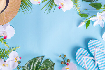Light blue colored summer vacation, travel and summer holiday background. Bright flatlay with tropical leaves and flowers, sea shells, starfish, flip-flops, hat, beach accessories, top view copy space