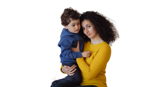 Calm Italian woman in yellow sweater, green pants sitting against transparent background, hugging son, looking at camera. Curly-haired European girl holds boy. Hispanic nanny takes care of curly child