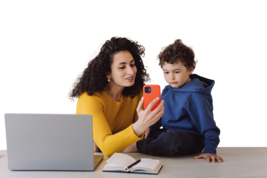 Brunette Italian woman in yellow sweater with braces sitting with little son against transparent background talks with grandparents by phone, makes video call. Curly housewife with adorable curly son