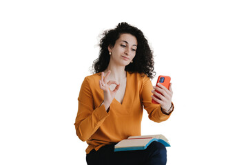 Naklejka premium Amused curly hispanic woman shows ok gesture during video call sits on sofa against transparent background. Beautiful arabic female in orange sweater confirms that is everything is good. Success