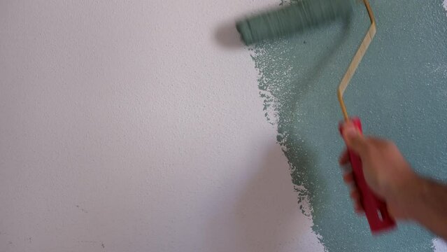 Man painting wall with green paint using roller. Construction worker, tool, apartment renovation.