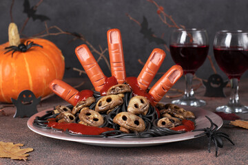 Themed food for Halloween - bloody hand from sausages with ketchup, mushrooms form of skulls and black spaghetti - obrazy, fototapety, plakaty
