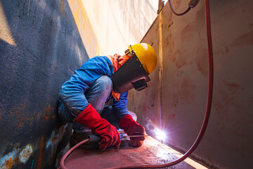 Male worker wearing protective clothing and repair welding industrial construction oil and gas or storage tank