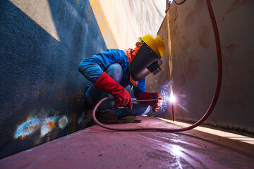 Male worker wearing protective clothing and repair welding industrial construction oil and gas or storage tank