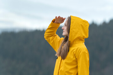 Pensive young woman in yellow jacket in nature looks into the distance. Forest on background. Side view. © somemeans