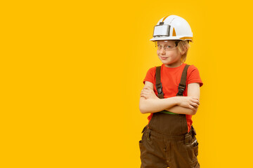 Portrait of smiling boy in protective helmet, glasses and jumpsuit like worker. Yellow background. Copy space, mock up