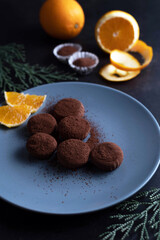 On a dark background, truffles in a plate, oranges and sprigs of greenery.