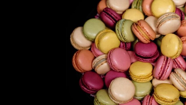 Top view of rotating fresh macaron cookies. Traditional french desserts from almond dough. Colourful sweet macaron cakes rotating against black background with copy space. French sweets concept.