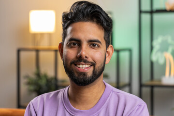 Obraz premium Portrait of happy calm indian man at home couch smiling friendly, glad expression looking away dreaming resting, relaxation feel satisfied concept good news, celebrate win. Hindu guy in living room