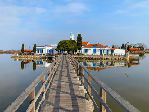 White church on a small island. The chapel of Panagia Pantanassa on quiet Vistonida lake in the morning sun. Old narrow wooden bridge joins it to historic Saint Nikolas Monastery. Xanthi, Greece.