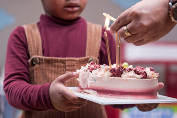 Africa American boy hold on celebrating her birthday cake and light a candle candles on cake in Kids birthday celebratiion party.