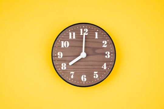 The Retro wooden clock at 8 O' clock on yellow color background.