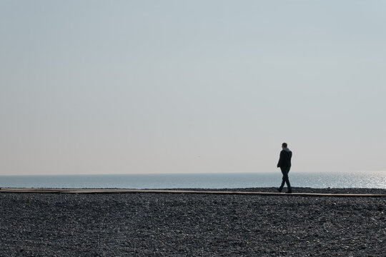 Man in silhouette walking on a boardwalk next to the Channel Sea