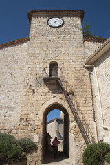 Femme touriste franchissant la tour d'entrée avec horloge dans la village de Laroque-Timbaud (Lot-et-Garonne)