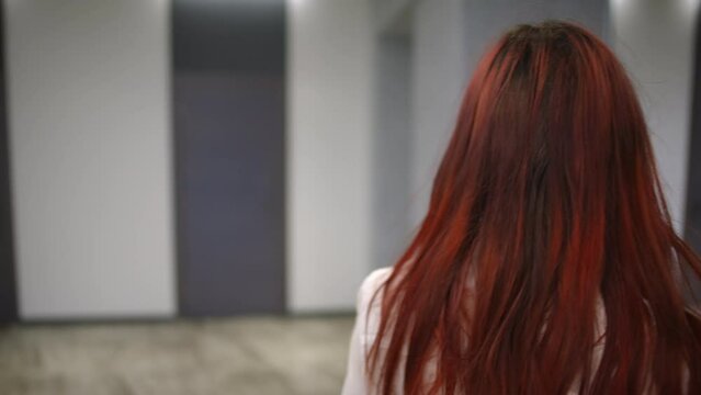 Back view close-up redhead young woman strolling in entrance lobby leaving. Live camera follows confident Caucasian lady walking in hallway indoors