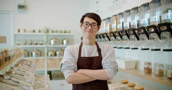 Portrait of happy asian man eco friendly shop owner smiling, looking at camera on plastic free grocery store background. Sustainable small local business startup go green market. Reduce Reuse Recycle.