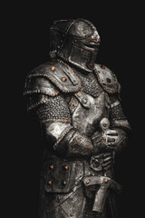 Statue of medieval knight in metal armor with a sword, isolated on dark black background