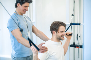 Young man having na physical therapy with instructor in the rehabilitation center