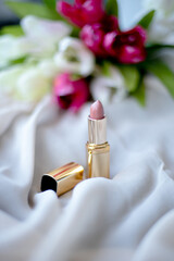 Lipstick in a gold case with flowers in the background. Lip makeup. Beauty concept.