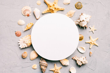 Summer time concept with blank greeting card and blank white paper on colored background. Seashells from ocean shore in the shape of frame separated with space for text top view