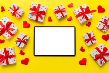 Top view of digital tablet with gift boxes and hearts on colorful background. Tablet with black screen with Holiday decorations gift box top view