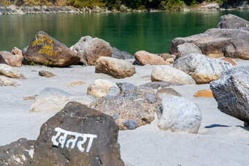 Fototapeta na wymiar Beautiful River Ganga near Rishikesh with stones and sand beach and Mountains. The inscription on the stone means Danger in Hindu. Pure natural clean river water.