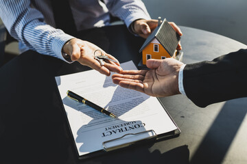 Real estate agent handing home keys to client after signing home purchase agreement. Signing real estate agreements, buying-selling, renting and mortgages.