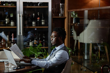 African American businessman typing contract on laptop while sitting at table in restaurant