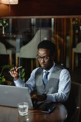 Vertical image of African American businessman working online on computer while sitting in coffee shop