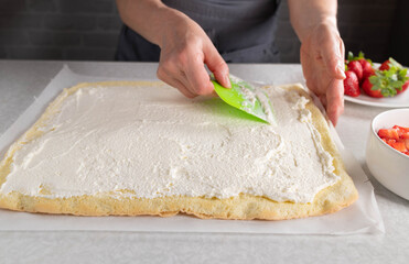 Woman spreads whipped cream on a sponge cake base for making a cake roll