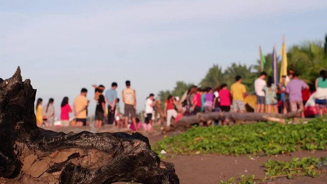 Religious congregations perform solemn worship on the sandy shore of a cheap resort during the hot summer. Burnt driftwood obscures the view.Blurs