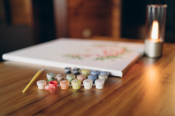Painting by numbers. A set for painting a picture, including a canvas, paints of different colors, brushes. Side view. Lamp in the background.