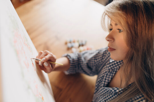 A girl in a shirt is painting with a brush on a canvas, drawing by numbers. Selective focus.