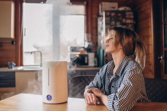 A Beautiful Woman Holds Her Hand Over A Diffuser With A Steamy Aromatic Oil On The Table In Her Home, Steam Coming Out Of The Humidifier. Selective Focus. Side View.