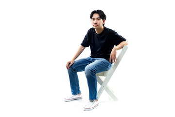 Studio shot of handsome asian young man in black t-shirt sitting on chair and looking at camera with smile isolated on white background