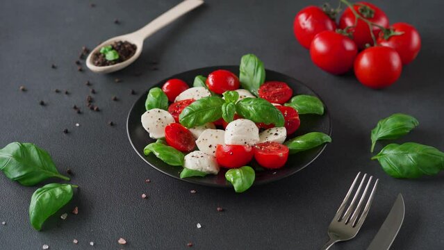 Caprese salad with ripe tomatoes and mozzarella cheese with fresh basil leaves on black background. Italian food