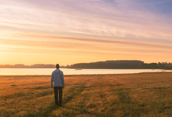 Young caucasian man in hoodie walking to pond under dramatic sunrise sky. Czech landscape