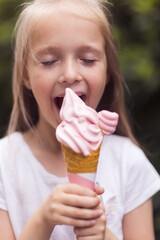 Pretty little caucasian girl with blonde hair eight years old eating licking vanilla ice cream in...