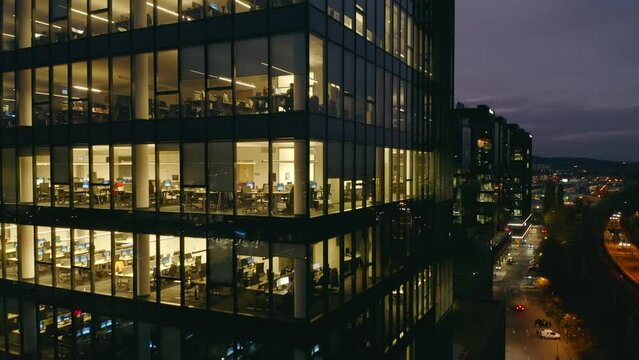 Aerial view of corporate office windows with workers at night. Cinematic shot drone on an office building at night, revealing the daily activities of office workers, night themes of late Generative AI