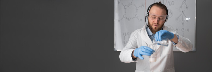 a chemistry teacher in white sits on a chair against the background of a marker board with...