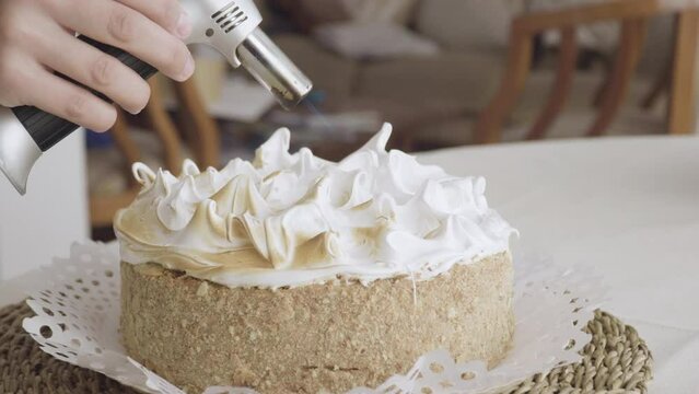close up on hand of pastry chef passing blowtorch on meringue topping of sheet cake