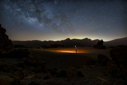Night time image of person exploring alien looking landscape with orange light torch and milky way starry sky backdrop in the national park of Minas de San Jose on Tenerife, Spain