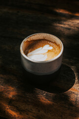 Ceramic mug with cappuccino on a dark wooden table. Delicious coffee with milk and foam in the sun