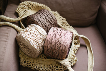 Three balls of knitted thread in an eco-friendly bag on a beige chair.
