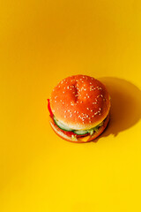 Delicious burger with sesame seeds on a yellow background, top view. Stylish concept of fast food and advertising burgers with fillings with space for text. Creative food mockup